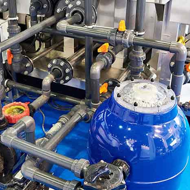 Système de filtration d'eau professionnel avec cuve bleue Système de filtration industriel avec tuyauterie grise en PVC, vannes oranges et grande cuve bleue brillante pour le traitement de l'eau.